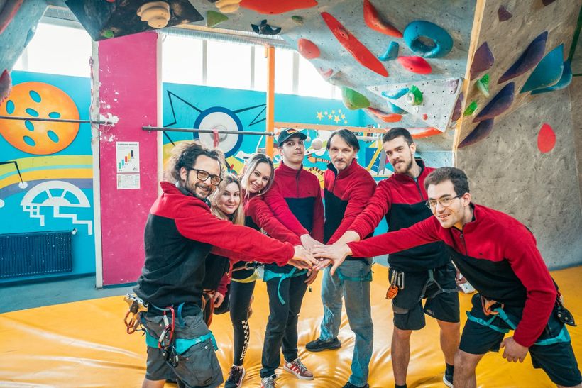 Grup de copii și instructori cu mâinile unite în cerc la sala de escaladă