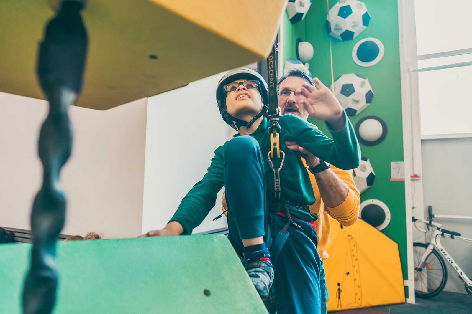 Copil cu cască de protecție ajutat de un instructor la peretele de escaladă Combretin